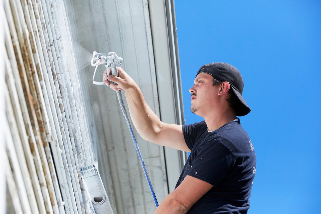 Man Spaying Paint On Exterior of Old Home